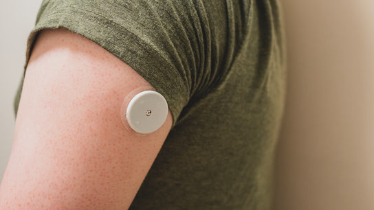 A round white medical sensor installed on the back of the upper arm. The sensor is descrete even though it’s installed just below the T-shirt line. The sensor is about the size of a chunky coin.