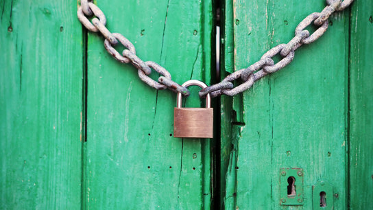 An old green door closed behind a padlock and chain.