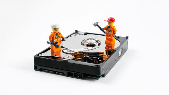 Two Lego brick figure construction workers stands on top of a hard drive with the hard disk drive platter exposed.
